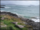 This is a color photograph of an Irish shoreline with waves crashing over the boulders.