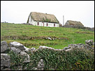 This is a color photo of one of the many thatched houses in Ireland, with a stone wall in front of it.