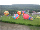 This is a color photo from up in a hot air balloon, seeing other balloons getting ready to take off.